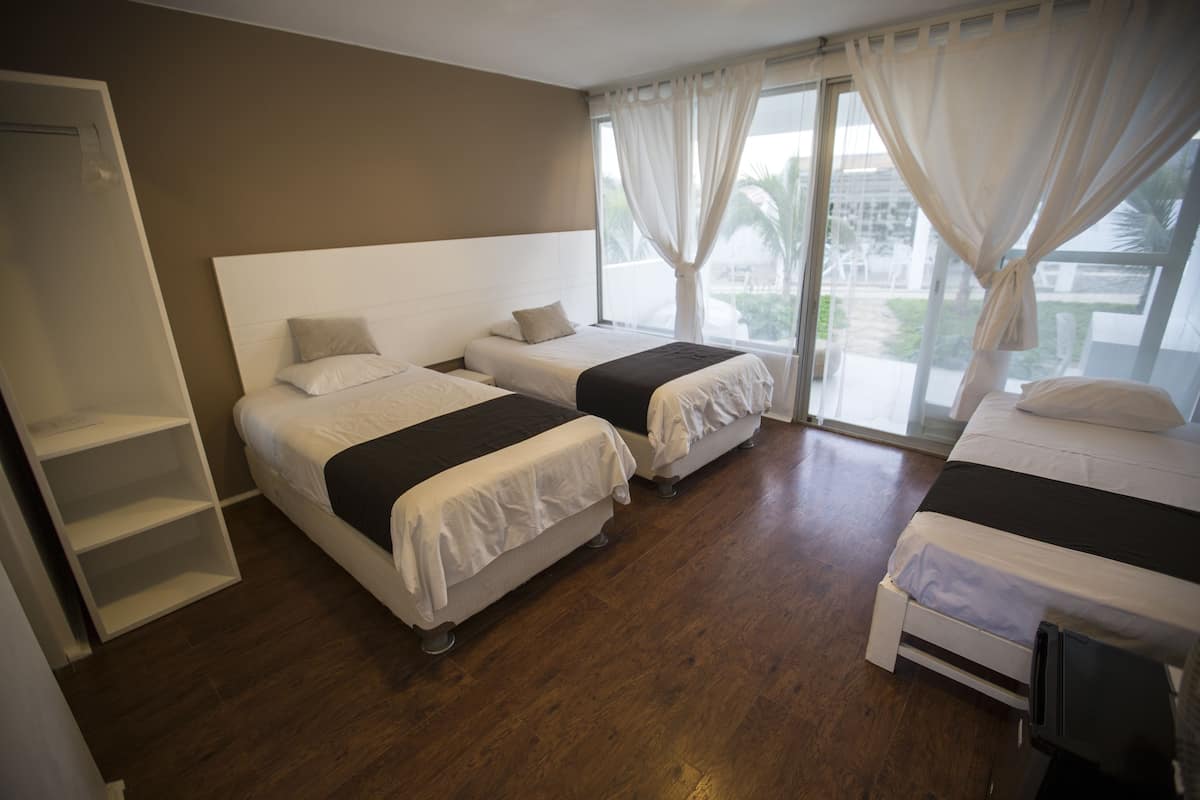 Habitación de hotel con dos camas, un armario y un ventanal con cortinas.