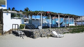 Una propiedad frente a la playa con piscina, sillas de descanso y un muro de piedra.