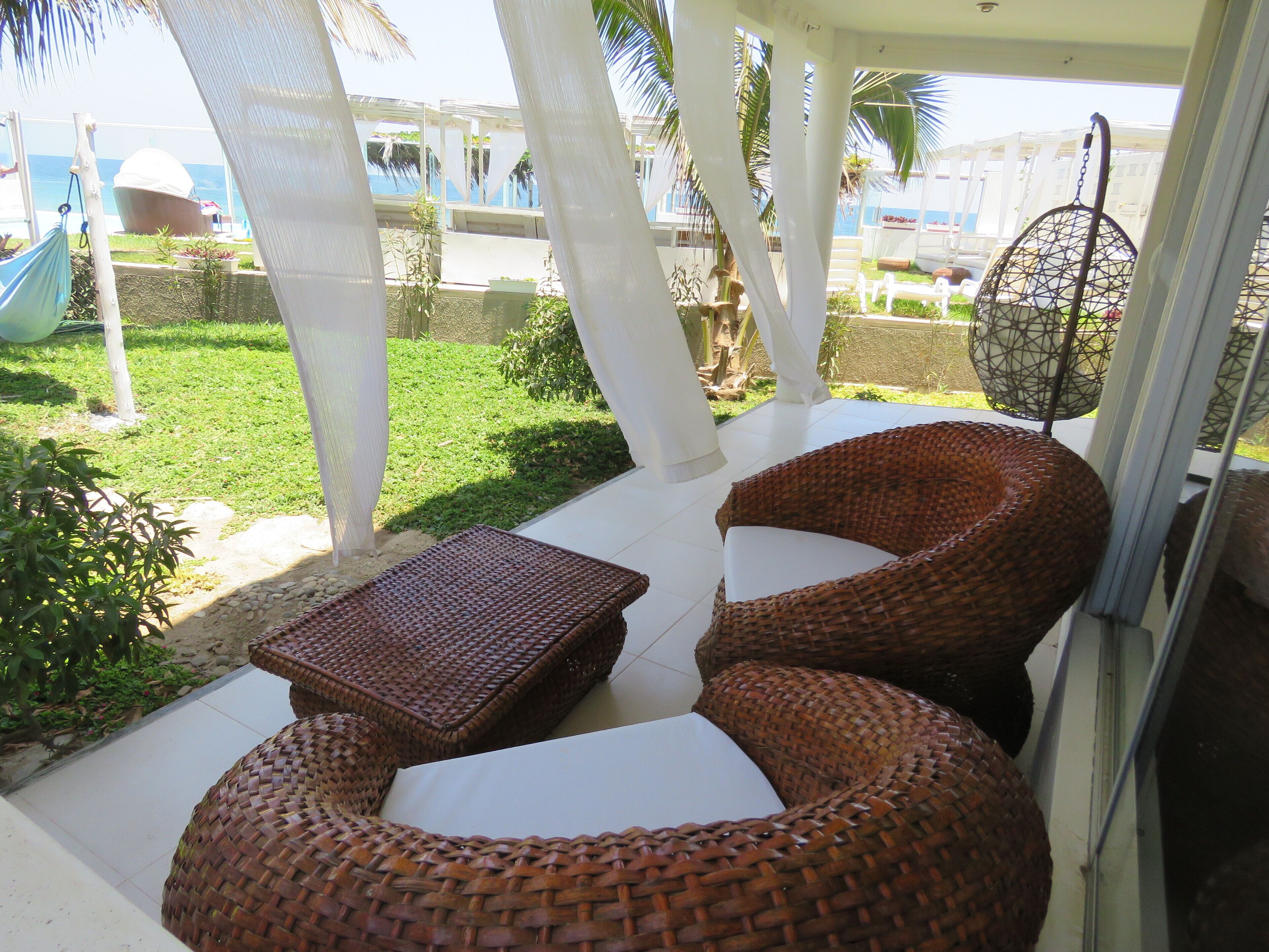 A covered patio area with wicker furniture, a small table, and a hanging chair.