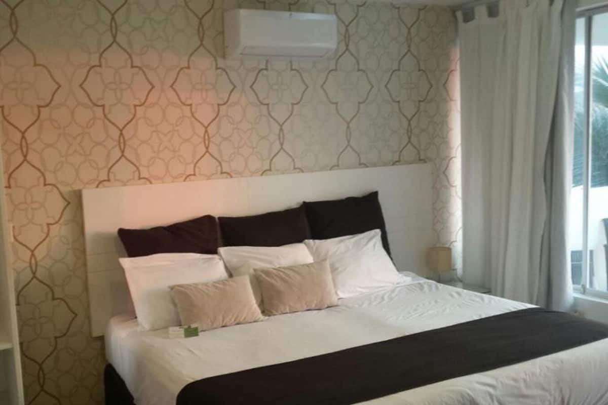 Habitación de hotel con cama, mesita de noche y ventana con cortinas.