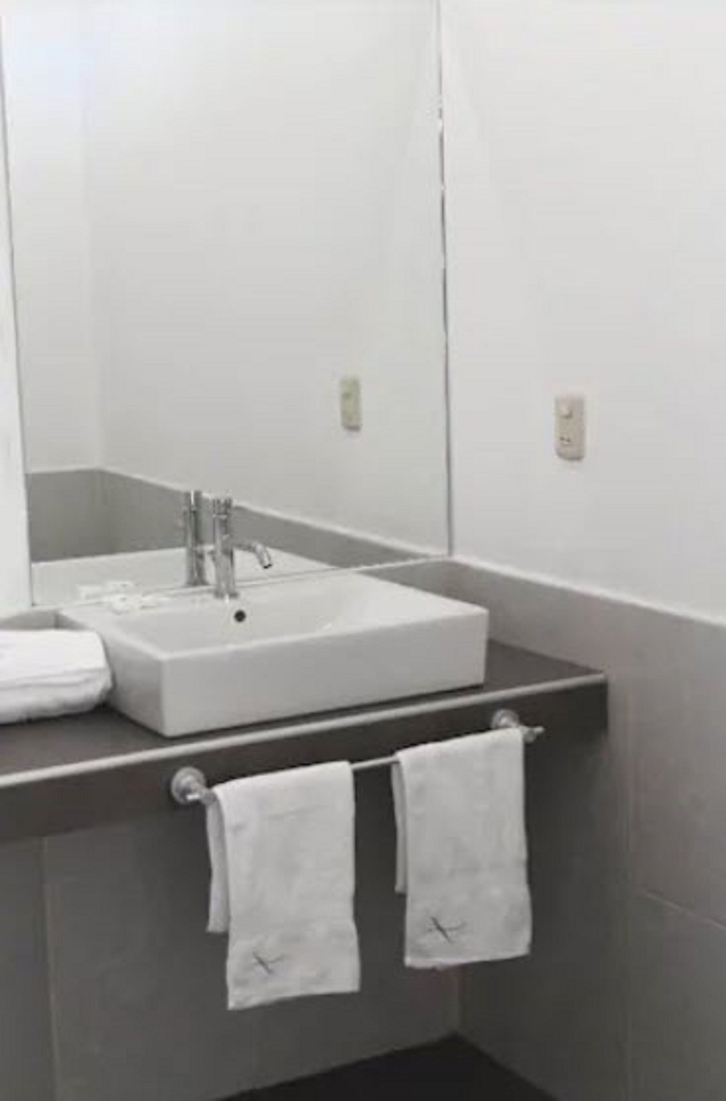 A bathroom with a white sink, a mirror, and two towels hanging on a rack.