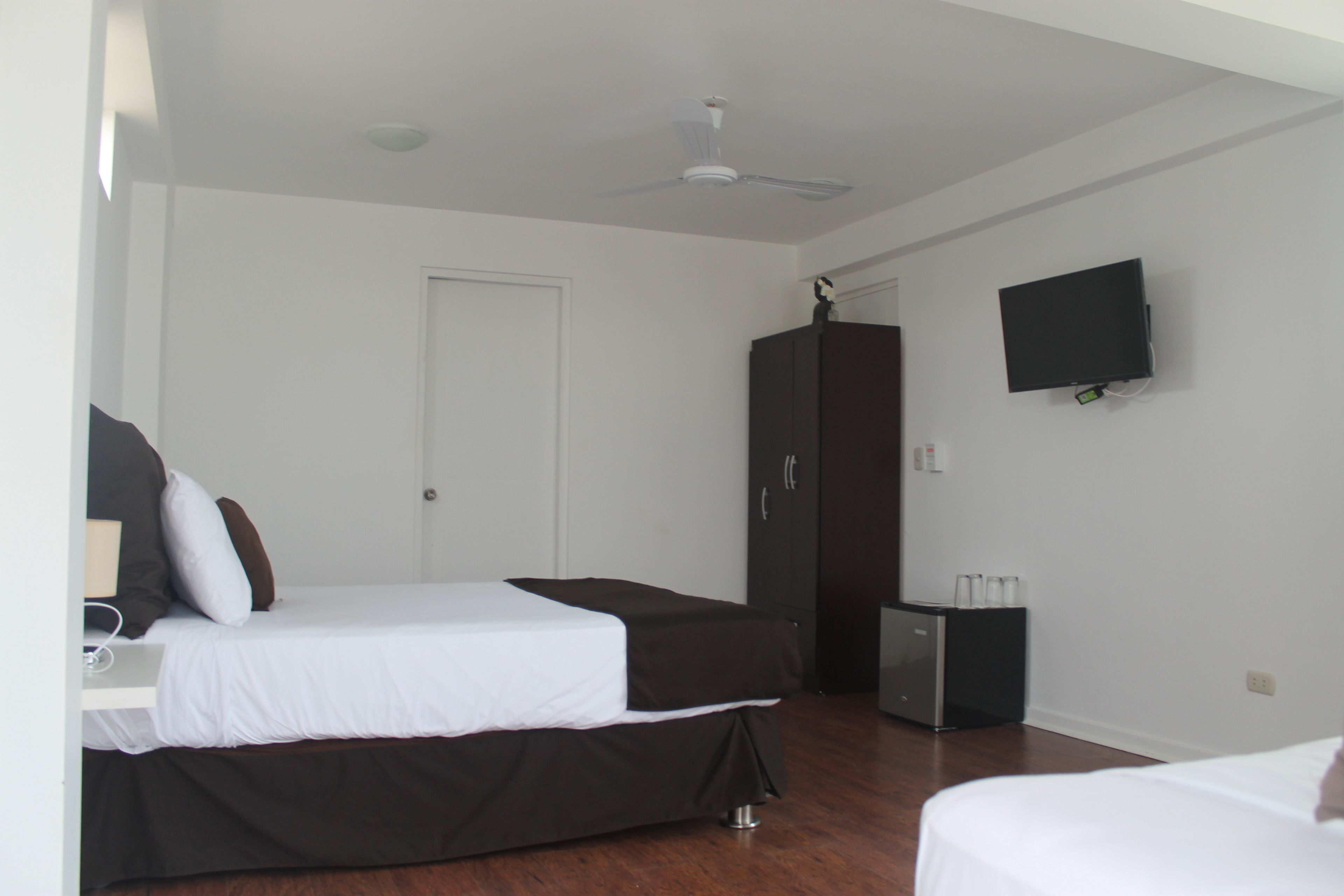 A hotel room with a bed, a wardrobe, a television, and a small table with a lamp.