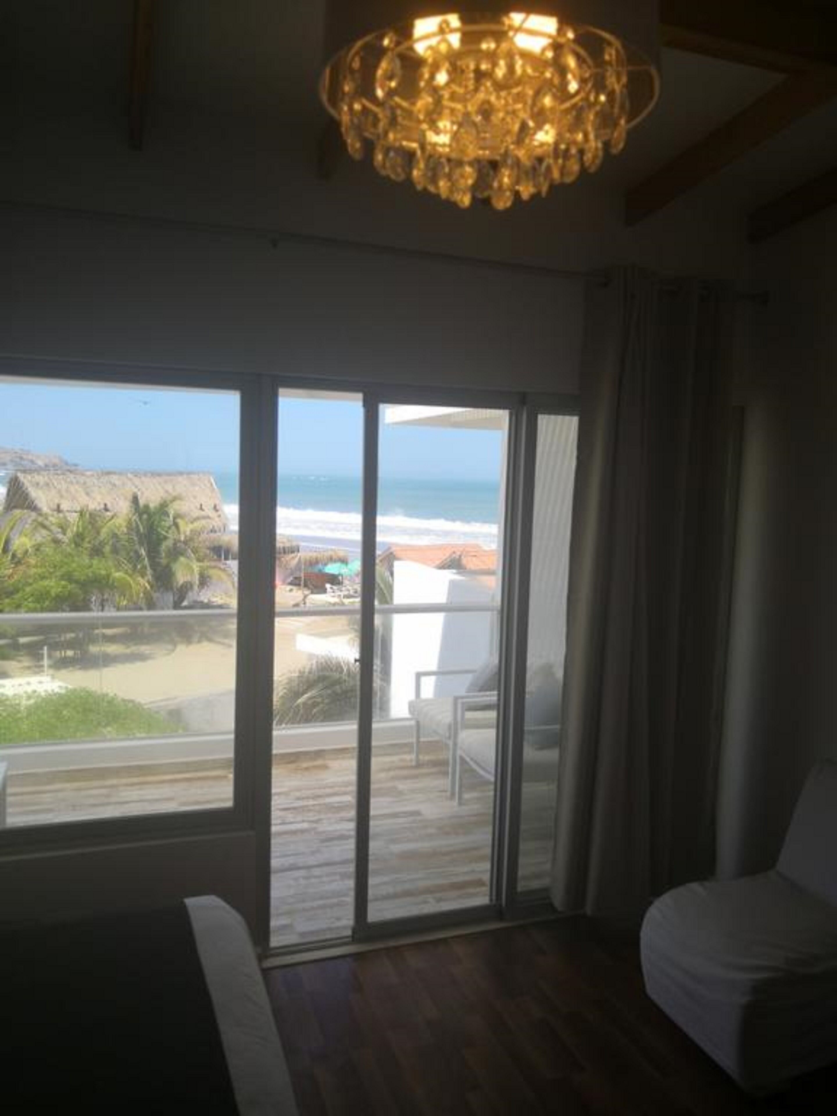 Una habitación con un gran ventanal corredero que da a un balcón con vistas a la playa y al océano.