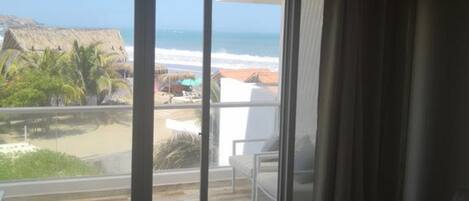 Una habitación con un gran ventanal corredero que da a un balcón con vistas a la playa y al océano.