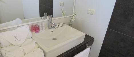 A bathroom with a white sink, dark tiles, a mirror, and a towel rack.