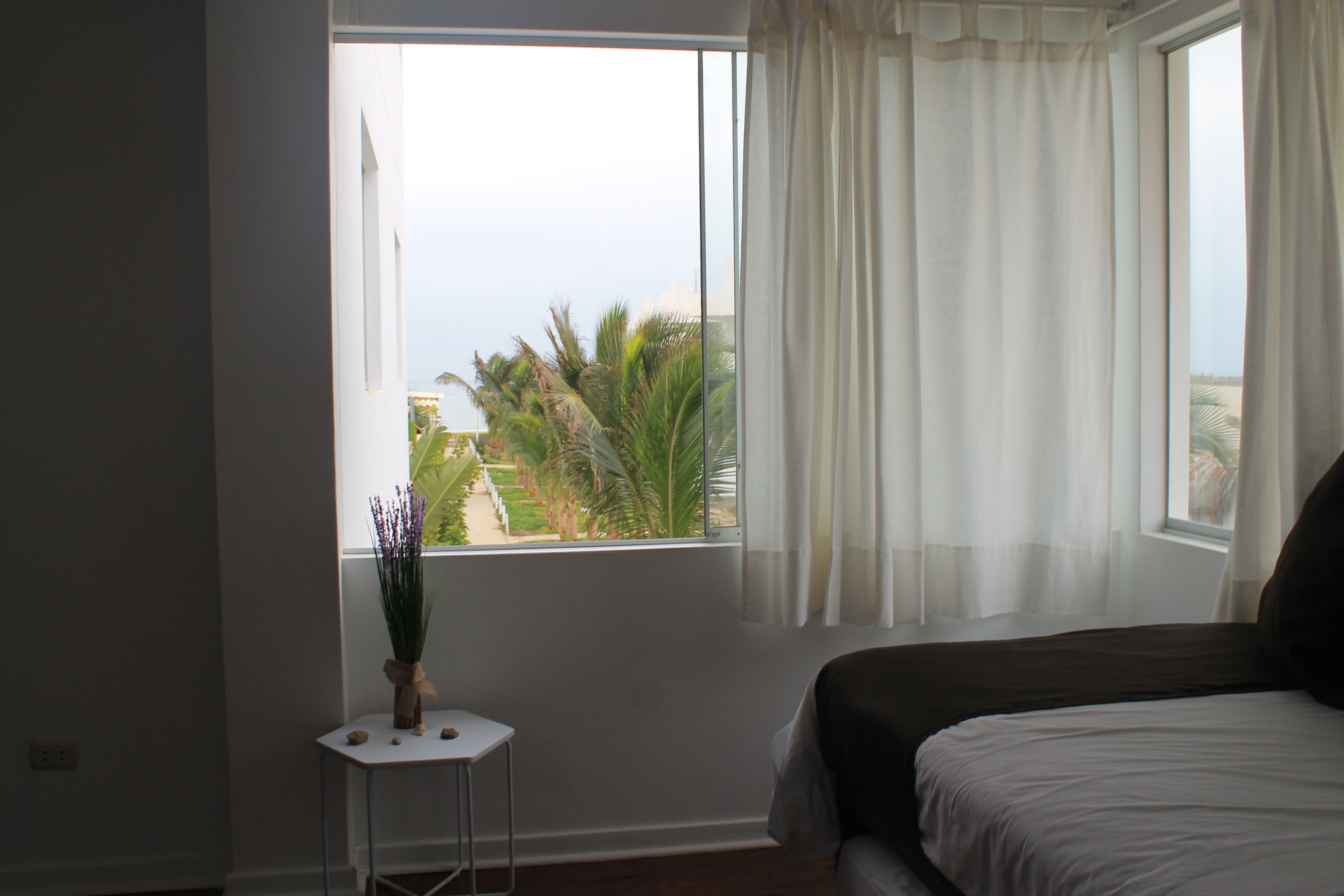 A bedroom with a large window, a bed, and a small table with a plant.