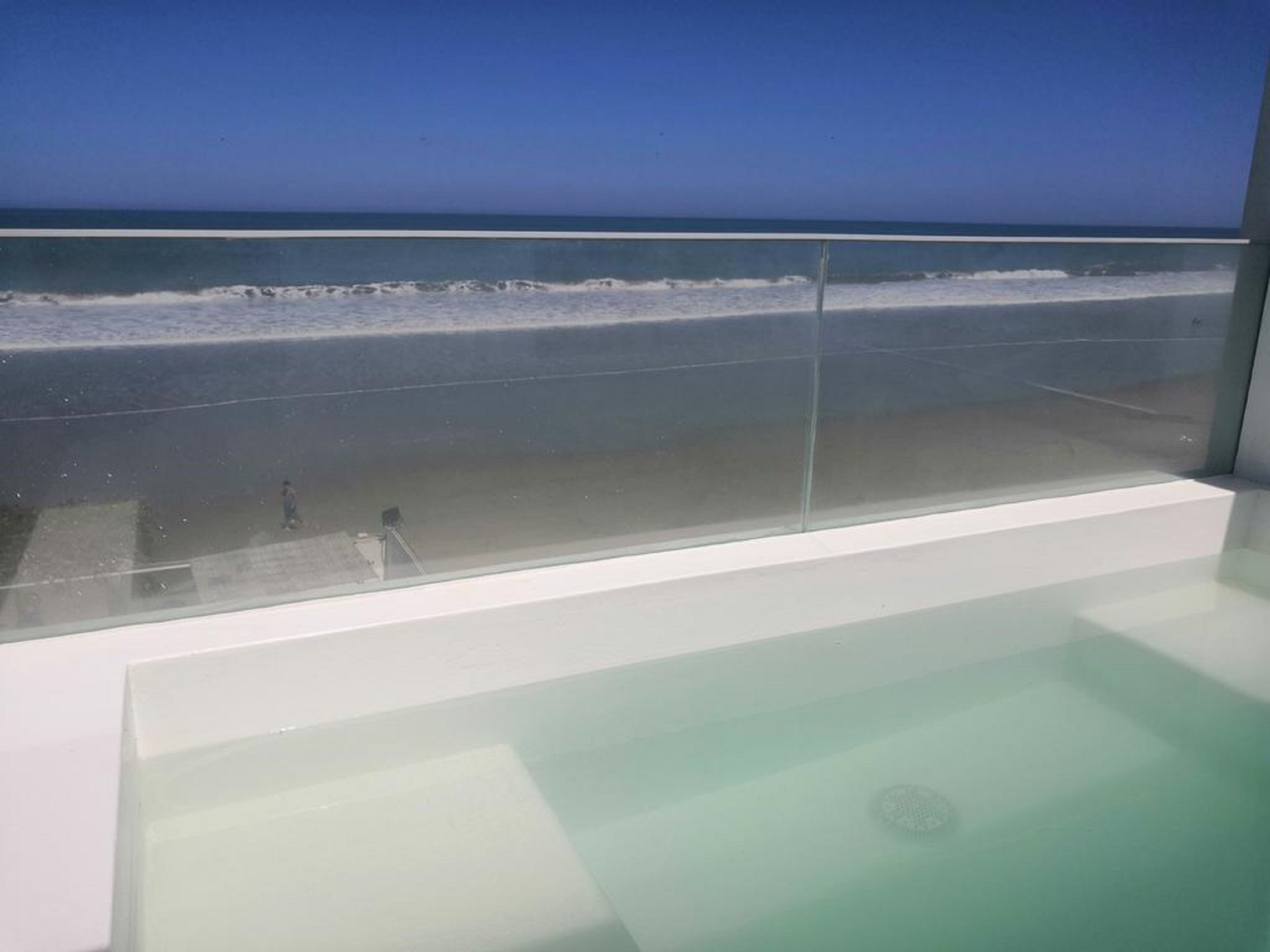Una bañera con paredes de vidrio y vistas a la playa y al océano.