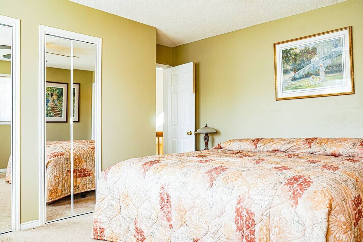 A bedroom with a bed, a mirror, a door, and a painting on the wall.