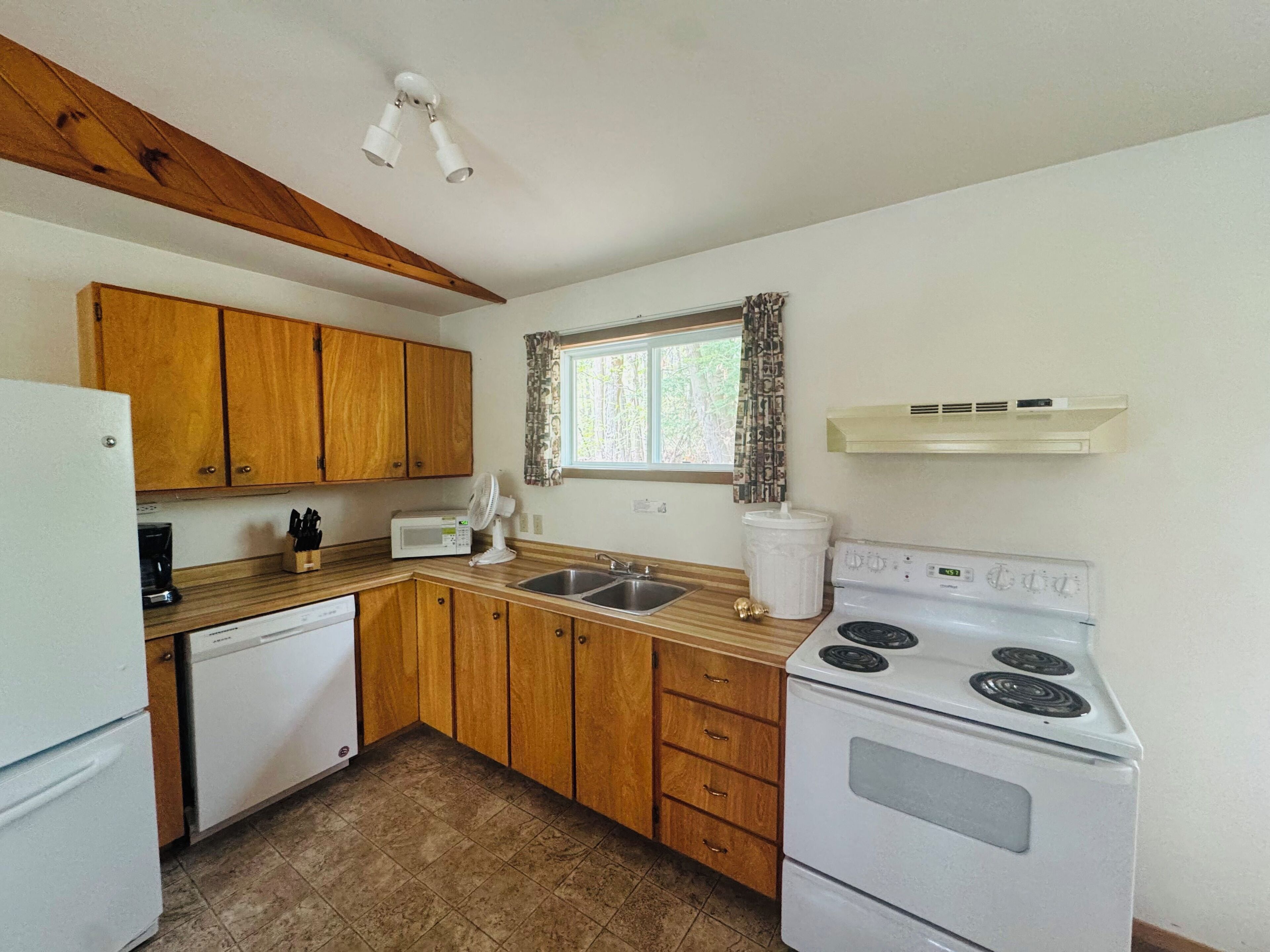 A compact kitchen with wooden cabinets, a white stove, a microwave, and a sink.