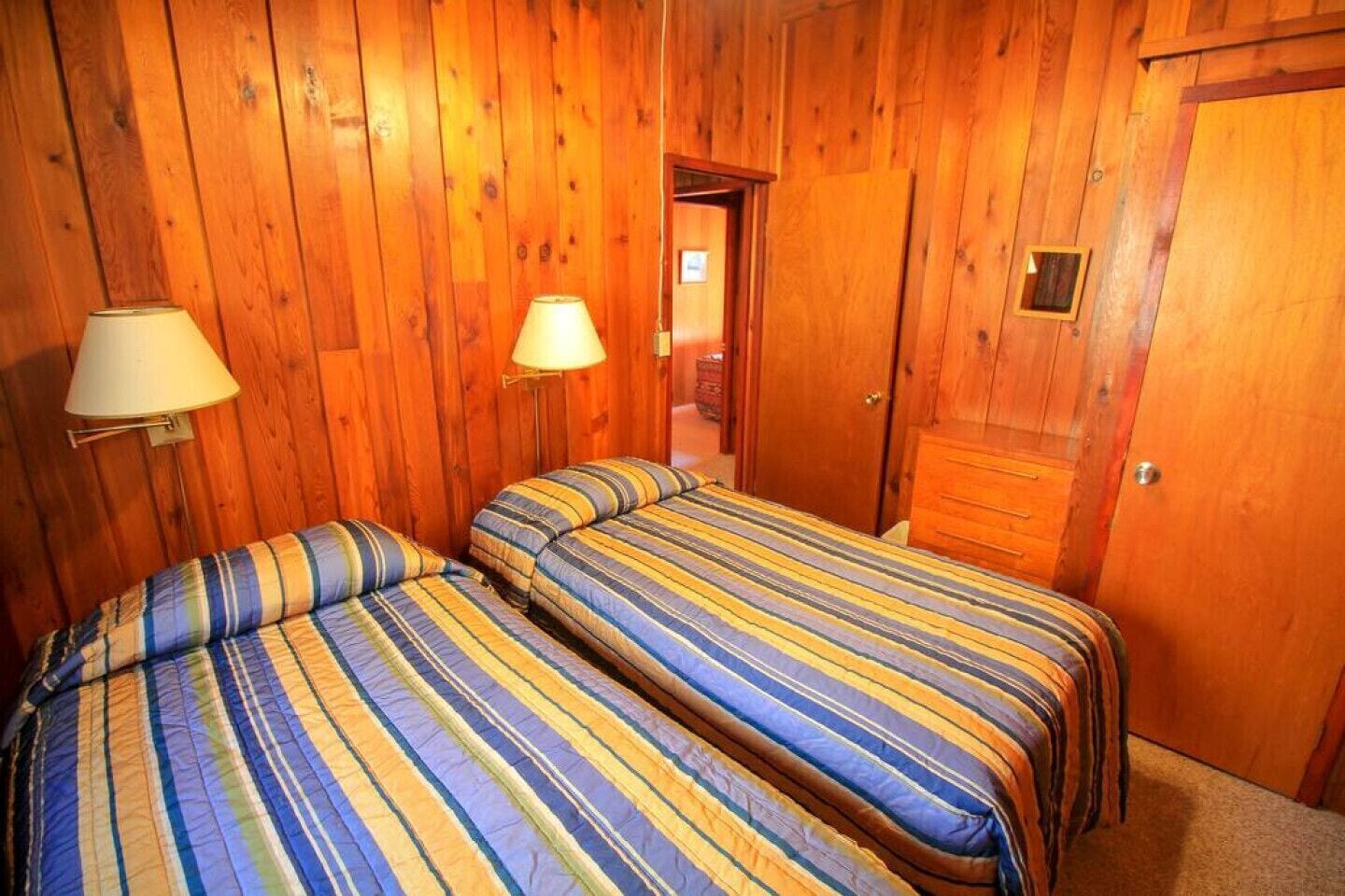 A room with two beds, wooden walls, a door, and a lamp.