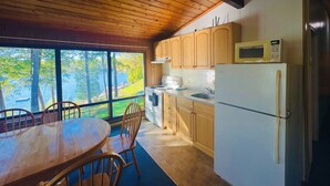 Une cuisine de style rustique, avec des meubles en bois, un réfrigérateur blanc et une vue sur une forêt grâce à de grandes fenêtres.