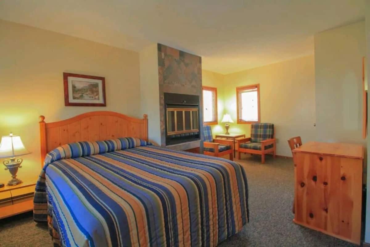 A bedroom with a bed, a fireplace, a desk, and a chair.