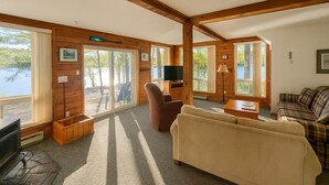 L’intérieur chaleureux d’un chalet avec une cheminée, un téléviseur et une grande fenêtre donnant sur un lac.