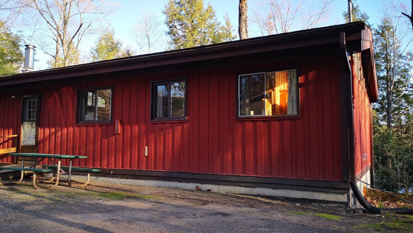 A red cabin with two windows, a chimney, and a picnic table.