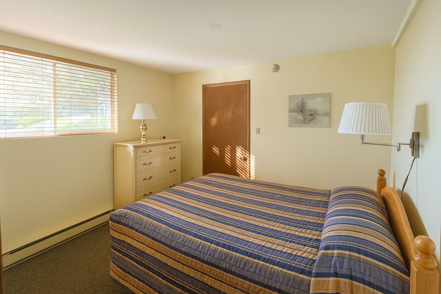 Un dormitorio con cama, cómoda, lámpara y una puerta.