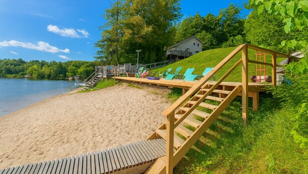 Une plage avec une terrasse en bois, des chaises longues et une maison en arrière-plan.