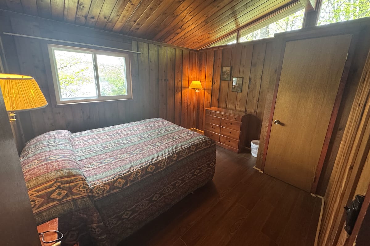 A wooden-paneled bedroom with a bed, dresser, and window.