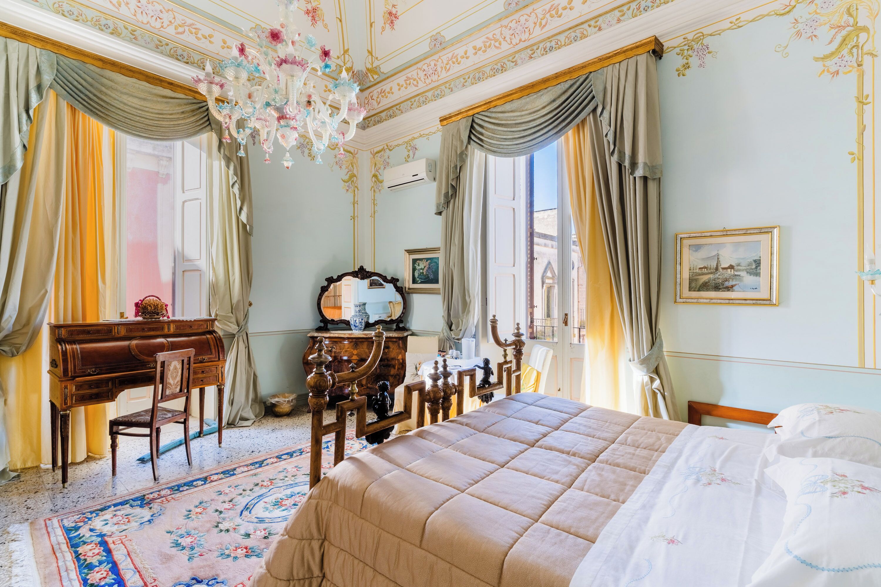 Una habitación con cama, escritorio, silla, cómoda y araña.