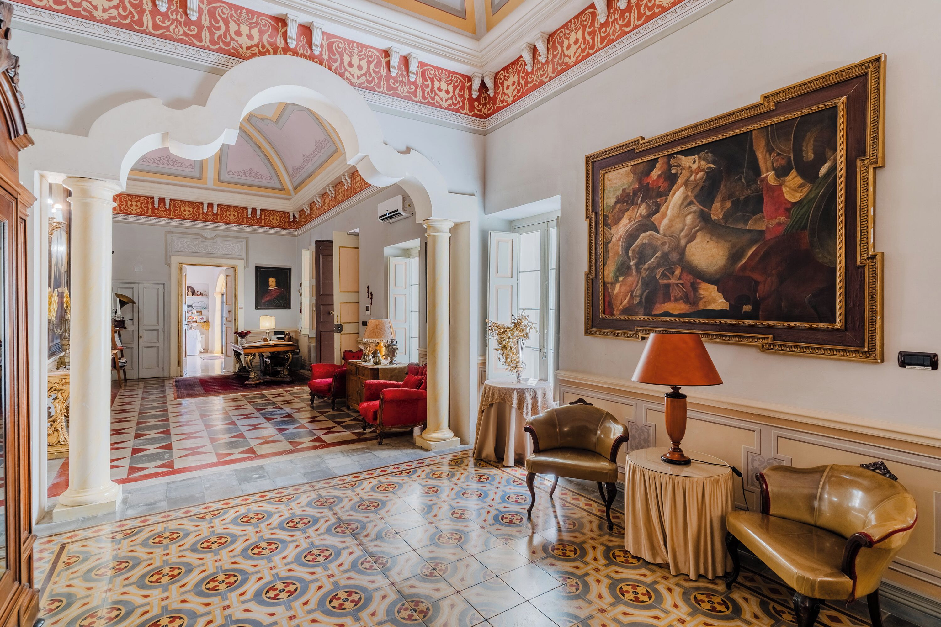 A spacious room with a patterned floor, a large painting on the wall, and a seating area with a table and chairs.