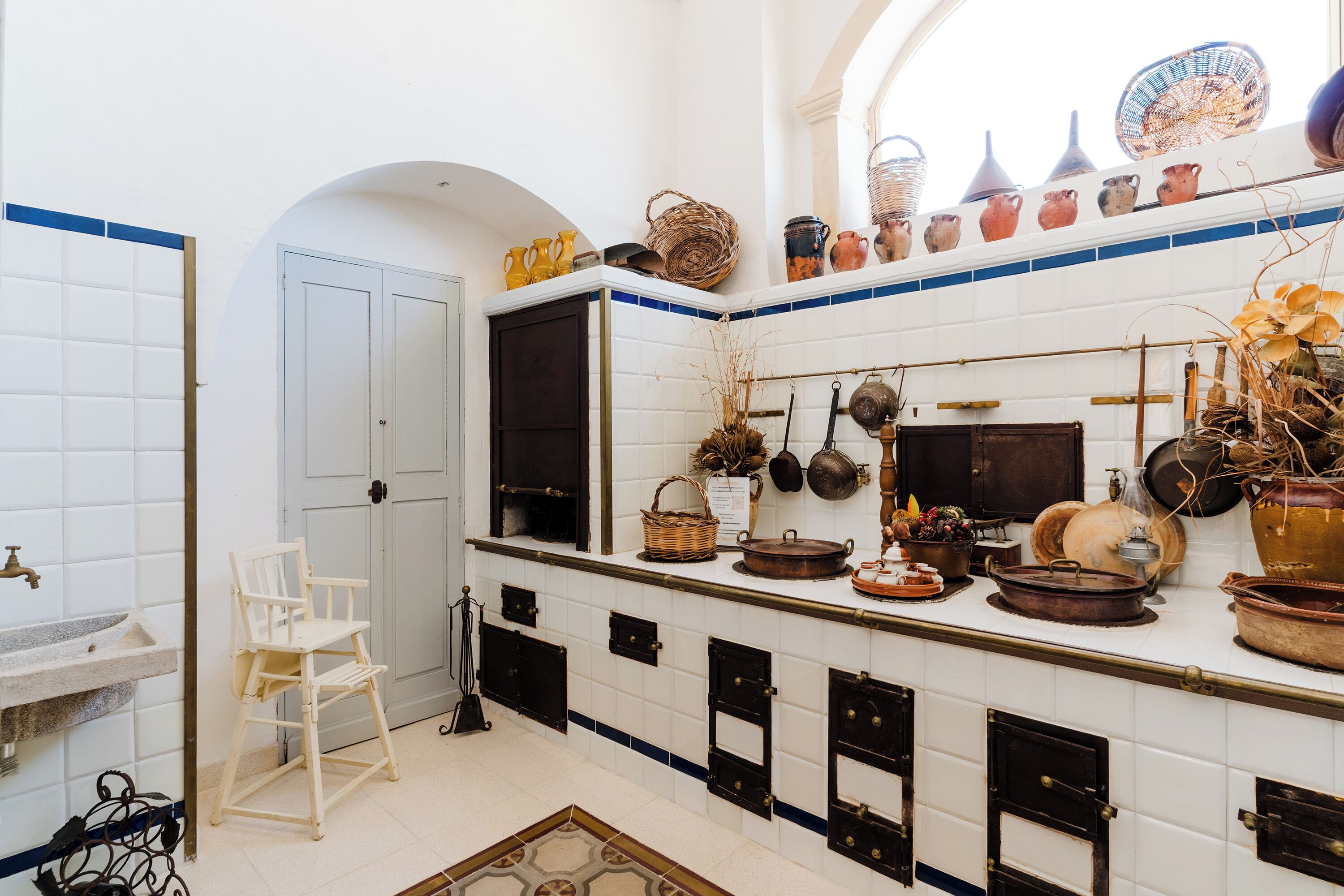 A kitchen with white tiled walls, a wooden chair, and various kitchen utensils and pots on the counter.