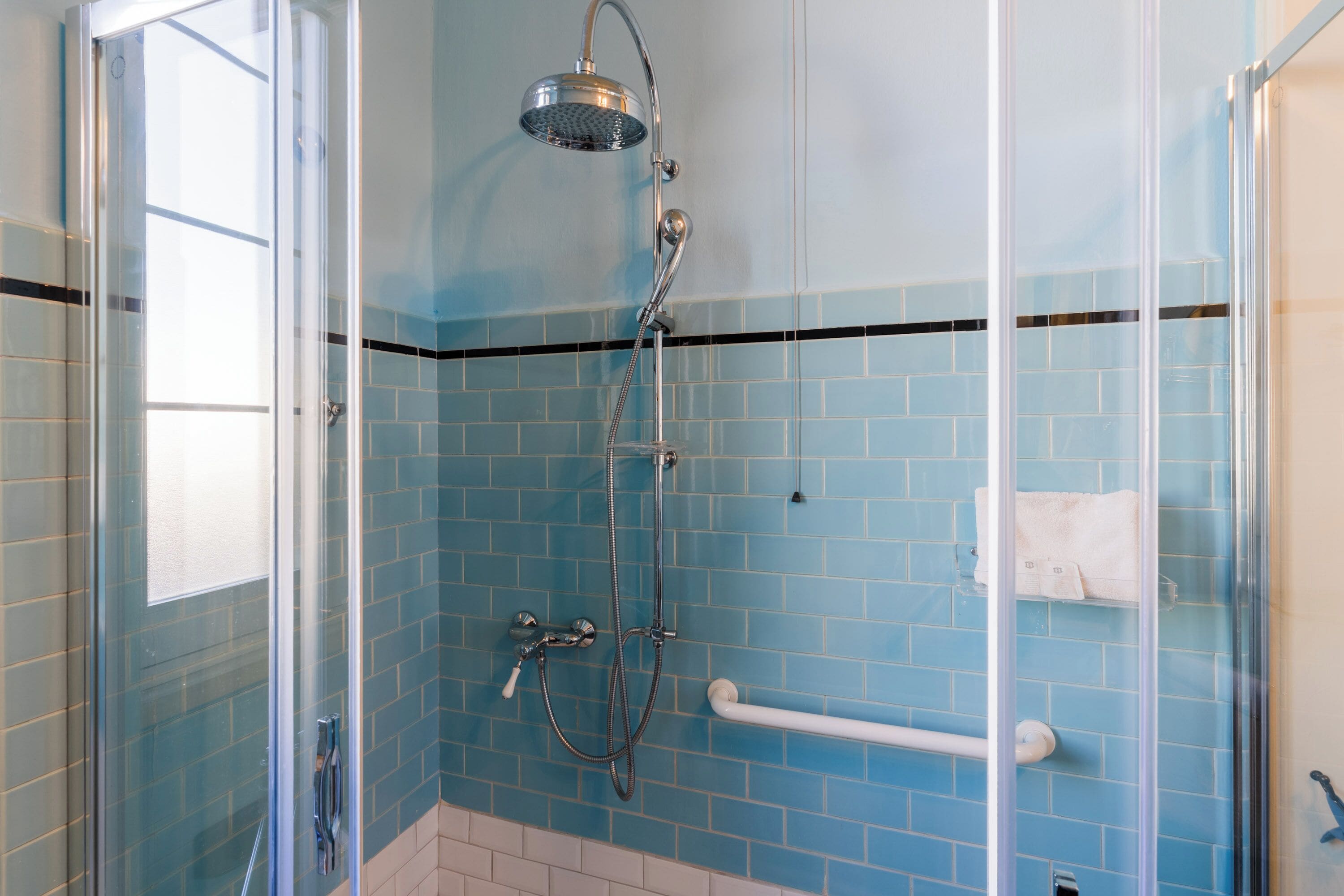 A bathroom with a glass shower enclosure, a handrail, and a towel rack.
