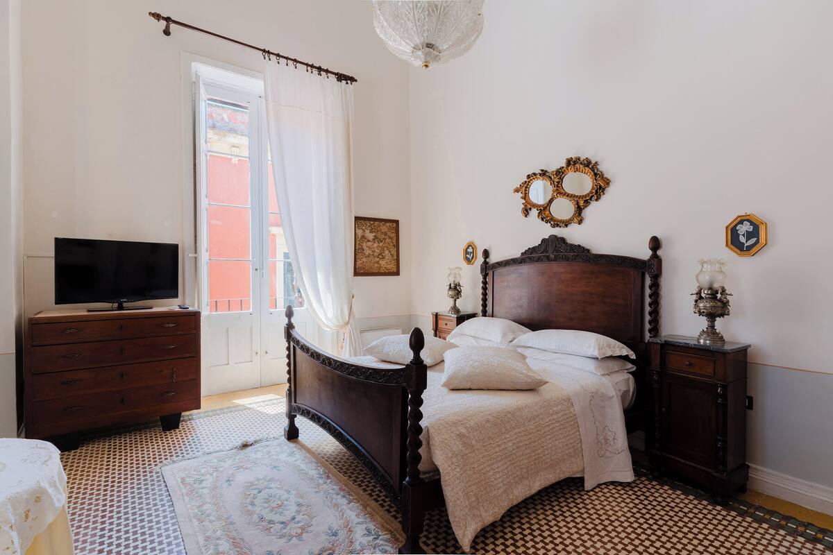 Un dormitorio con una cama de madera, un aparador, un televisor y una alfombra estampada.