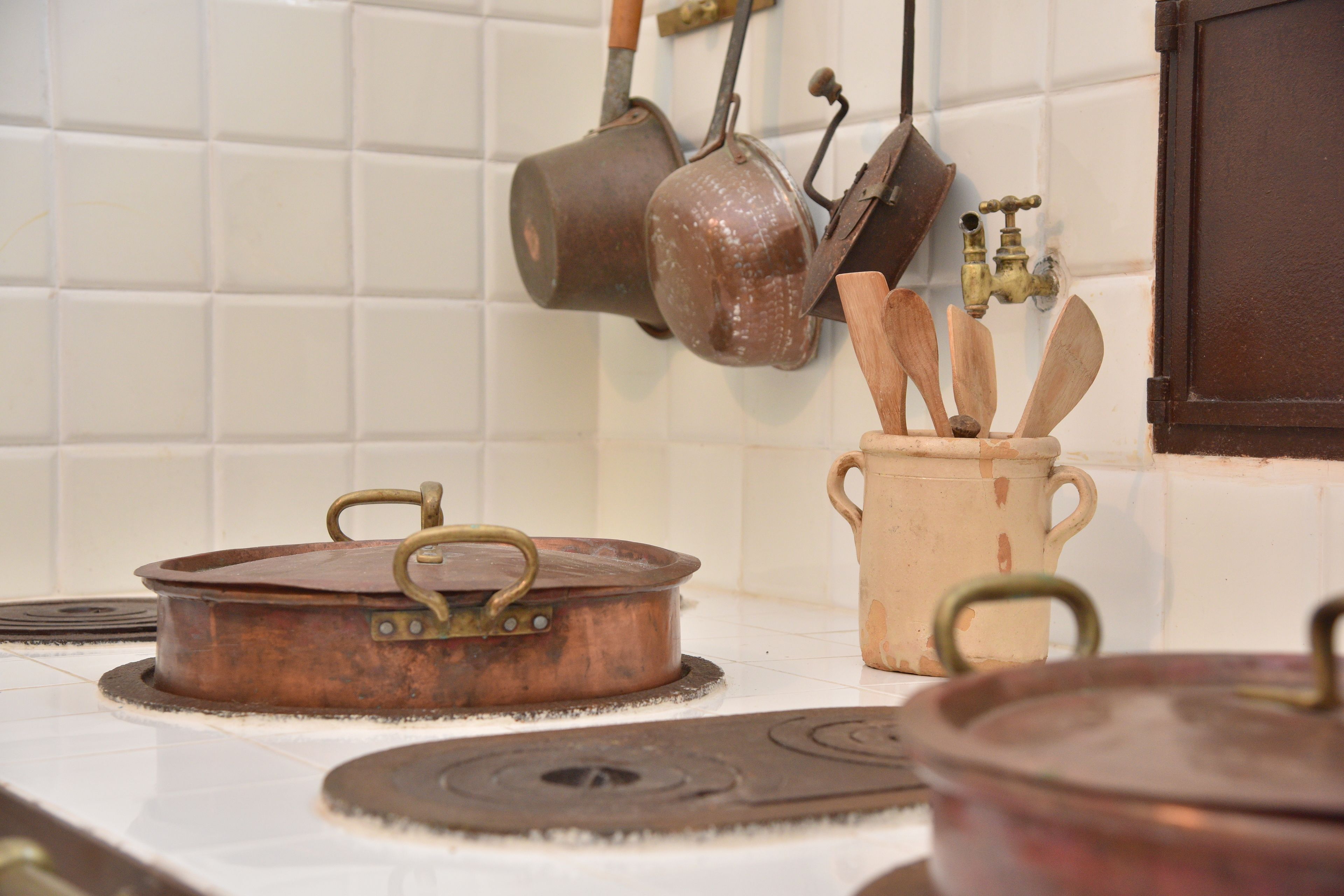 A kitchen with white tiled walls, a stove, and hanging pots.