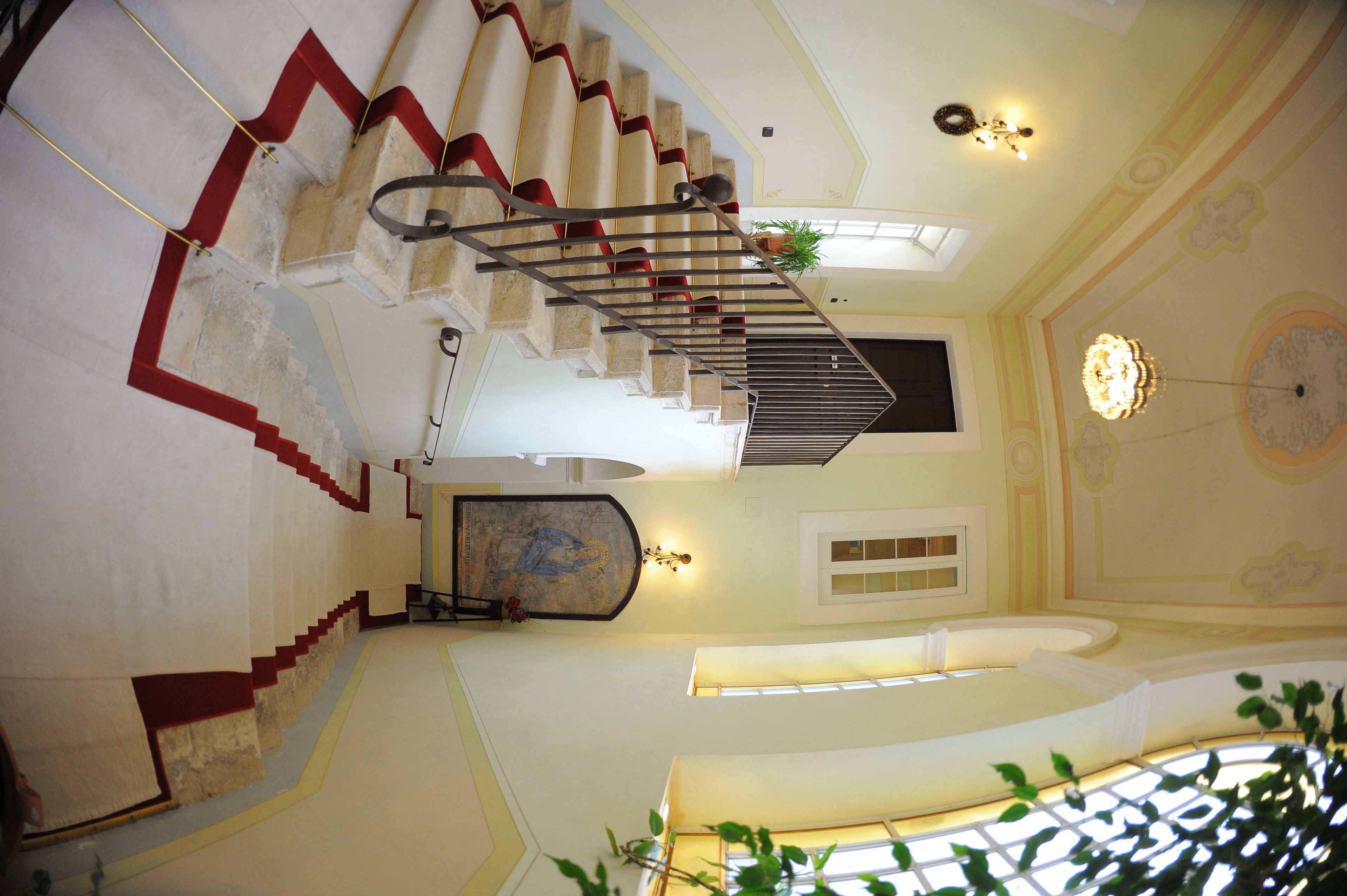 Eine prächtige Treppe mit rotem Teppich, einem Chandelier und einem Gemälde an der Wand.