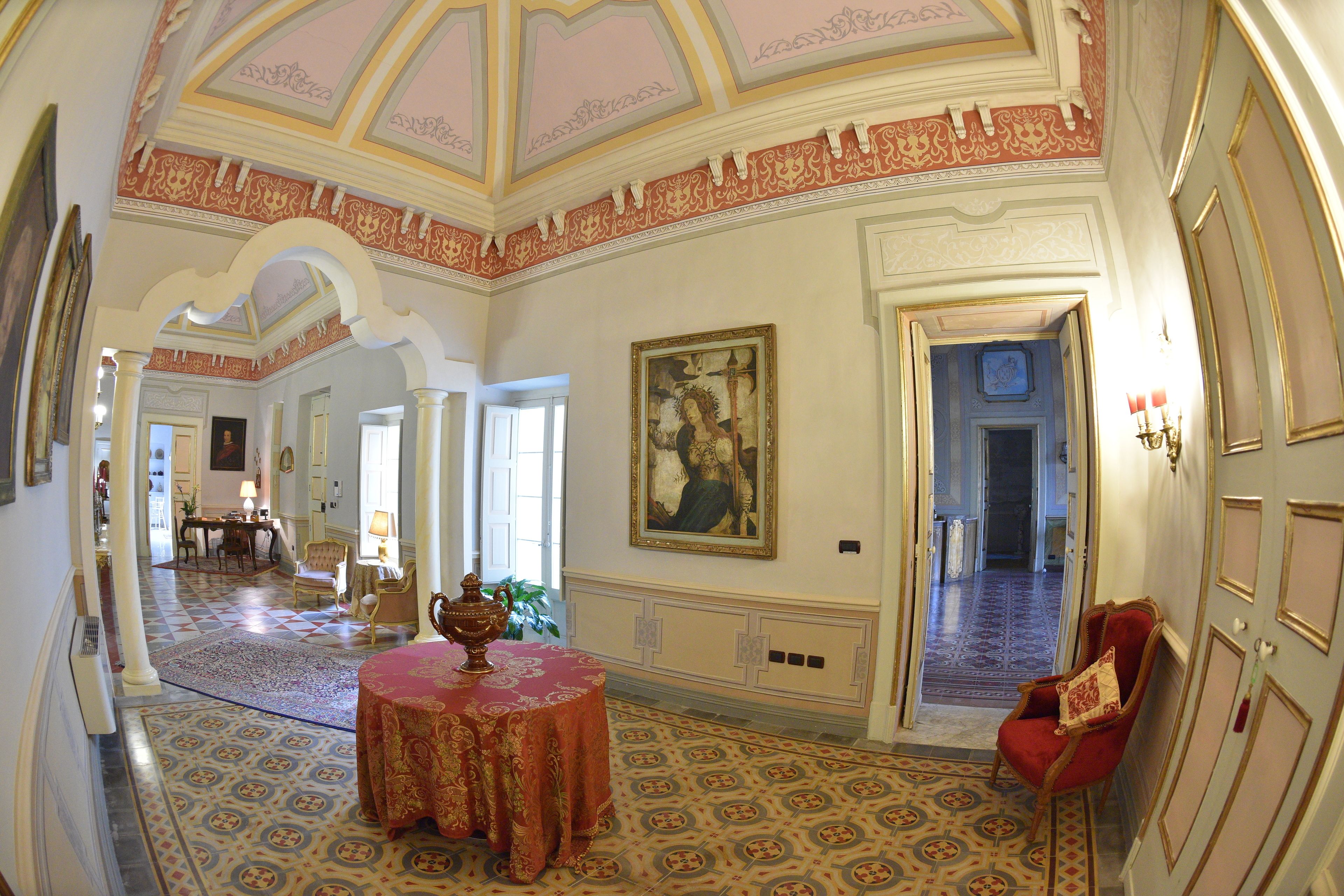 Un vaste hall d’entrée avec un plafond richement décoré, un grand tableau et un fauteuil rouge.