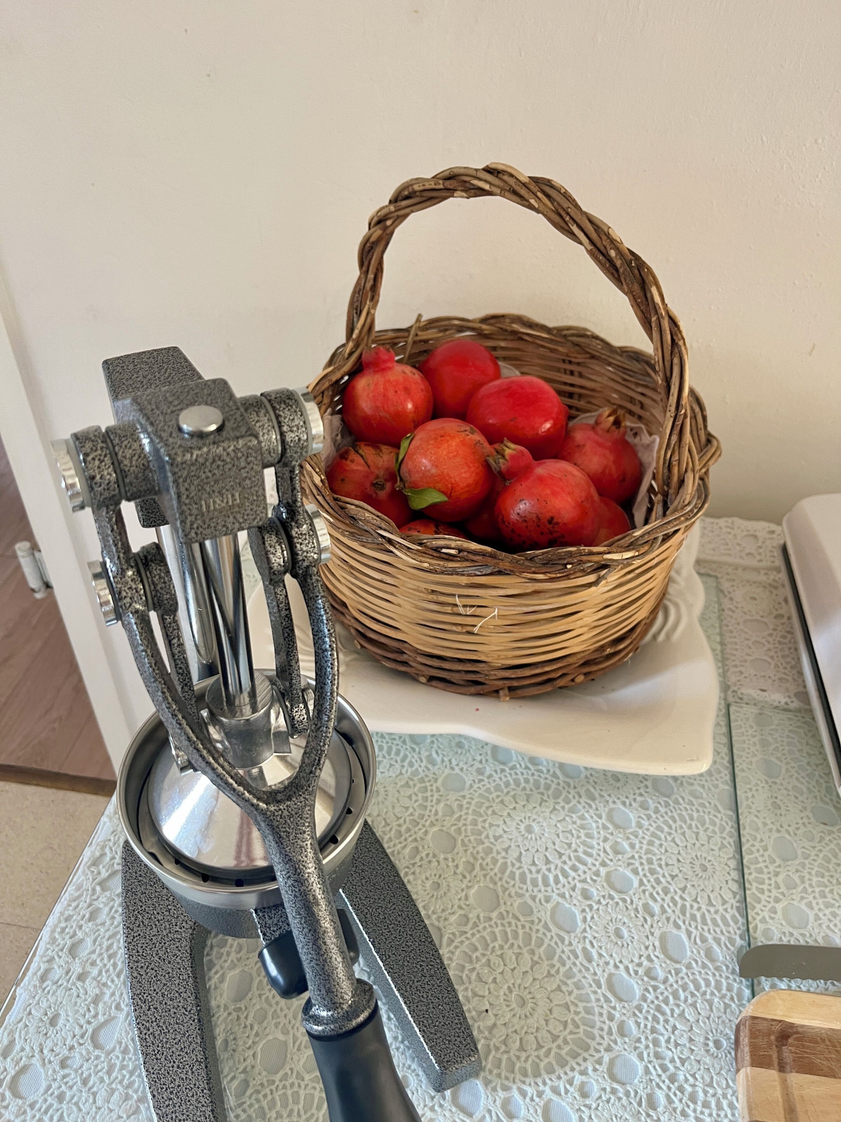Et køkken med en frugtpresse og en kurv granatæbler på et bord.