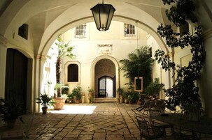 Un patio arqueado con suelo de adoquines, plantas en macetas y un farol colgante.