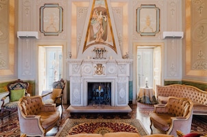Una sala imponente con chimenea, sillones ornamentados y una araña.