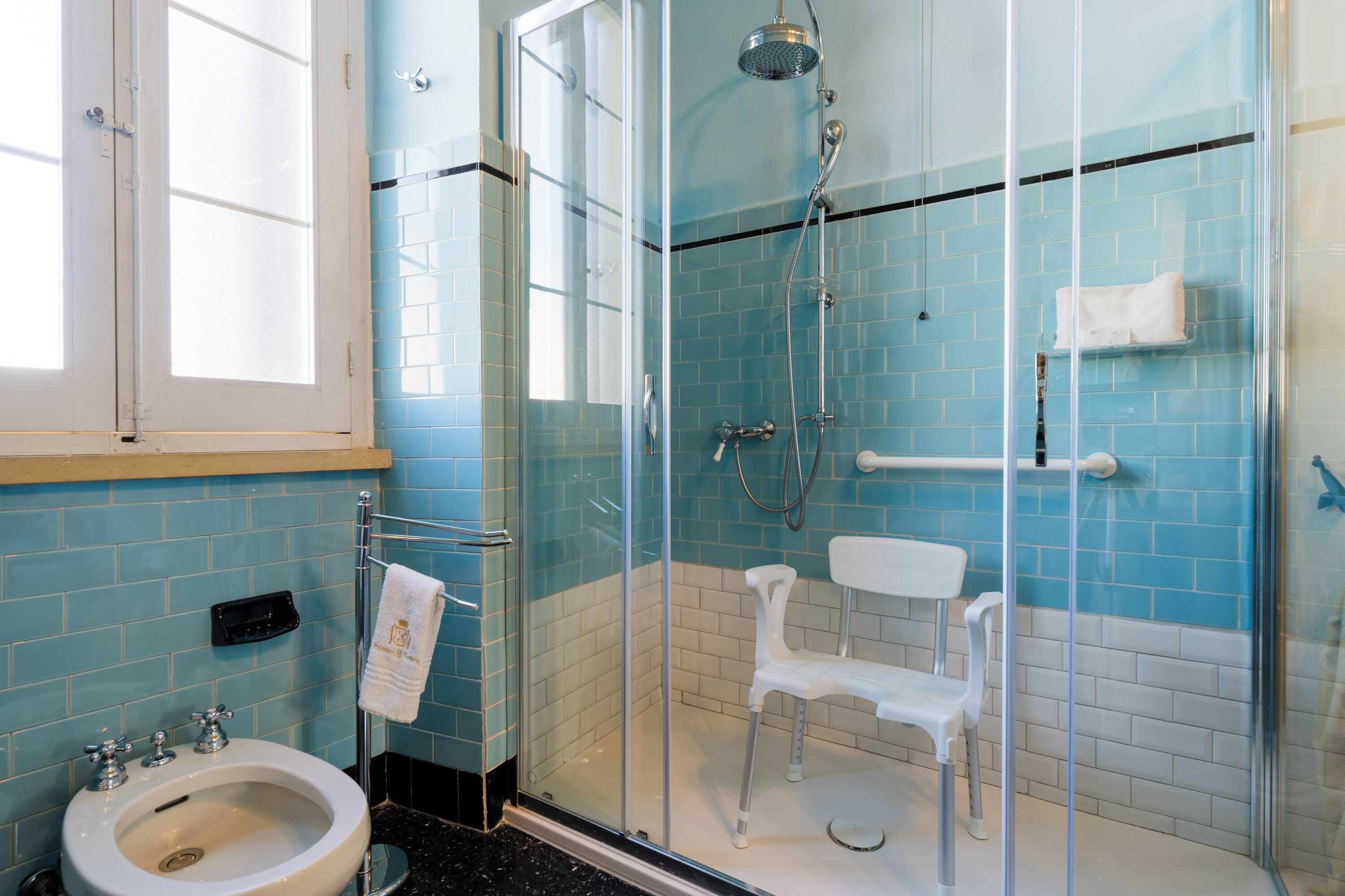 Un baño con ducha envuelta en vidrio, un lavamanos blanco y un perchero para toallas.