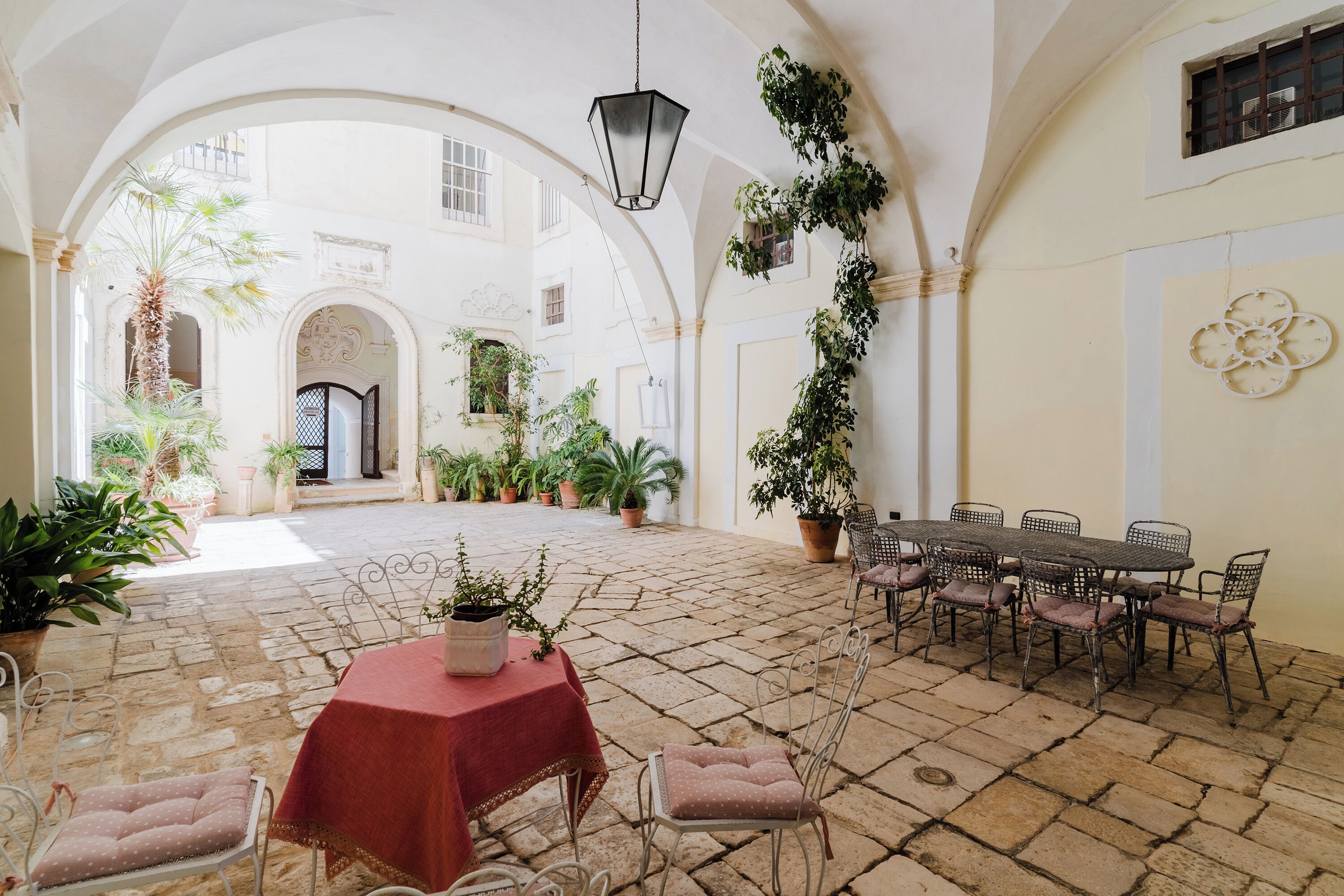 Un pati amb una taula i cadires, envoltat d'arcs i plantes en testos.