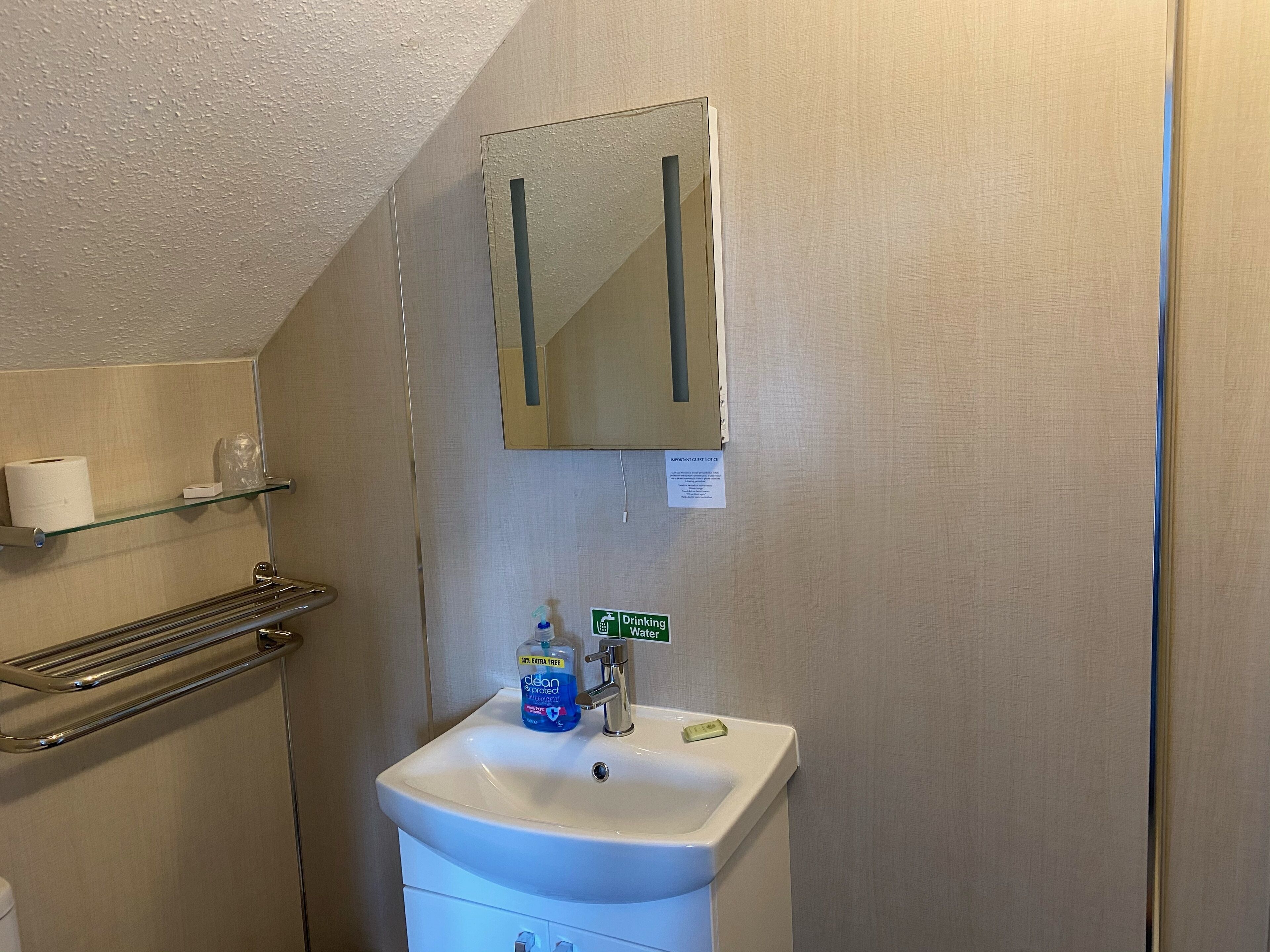 A bathroom with a white sink, a mirror, a towel rack, and a sign indicating a drinking water station.