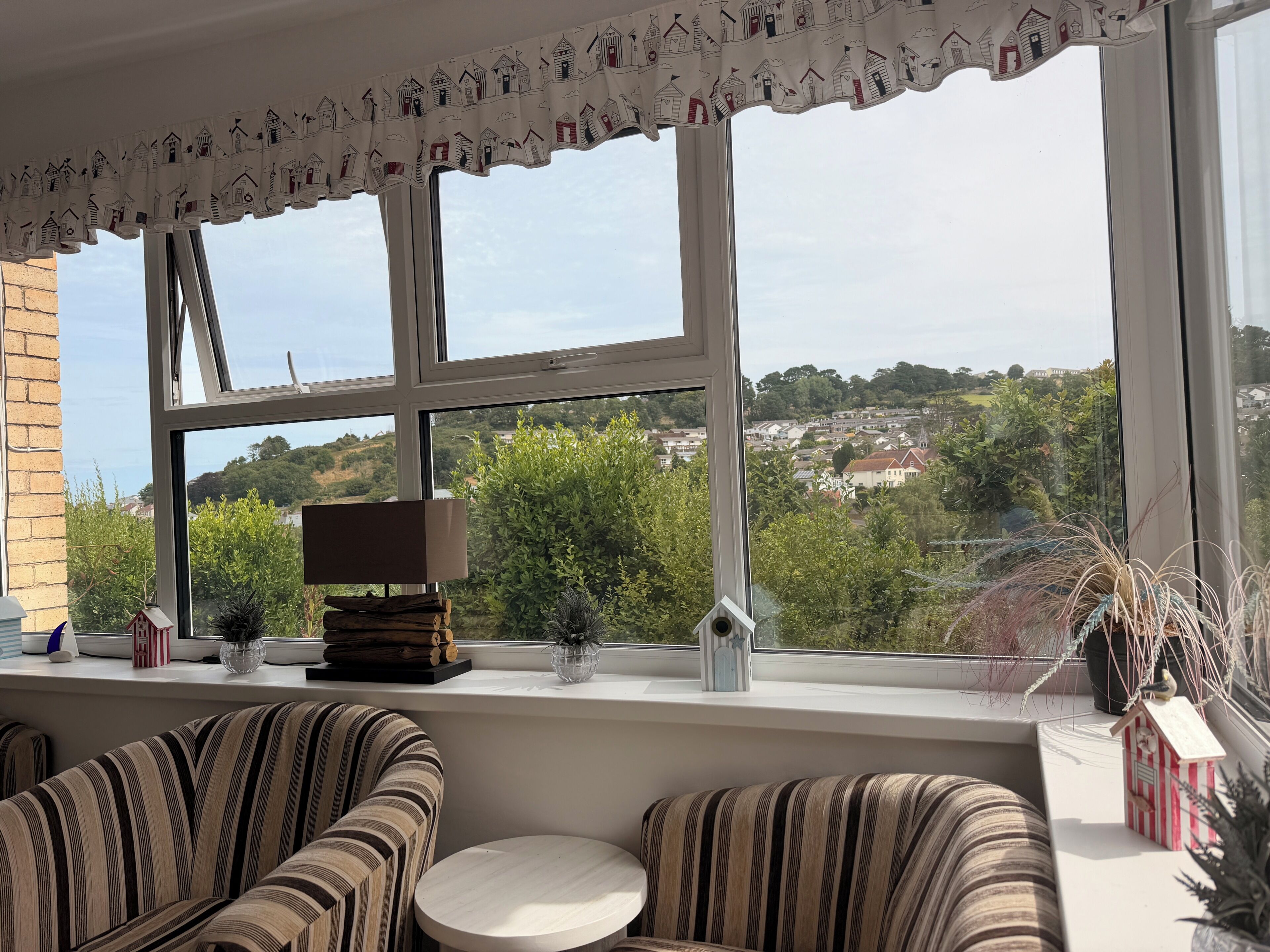 A room with a large window, striped upholstered chairs, a small round table, and a decorative window valance.