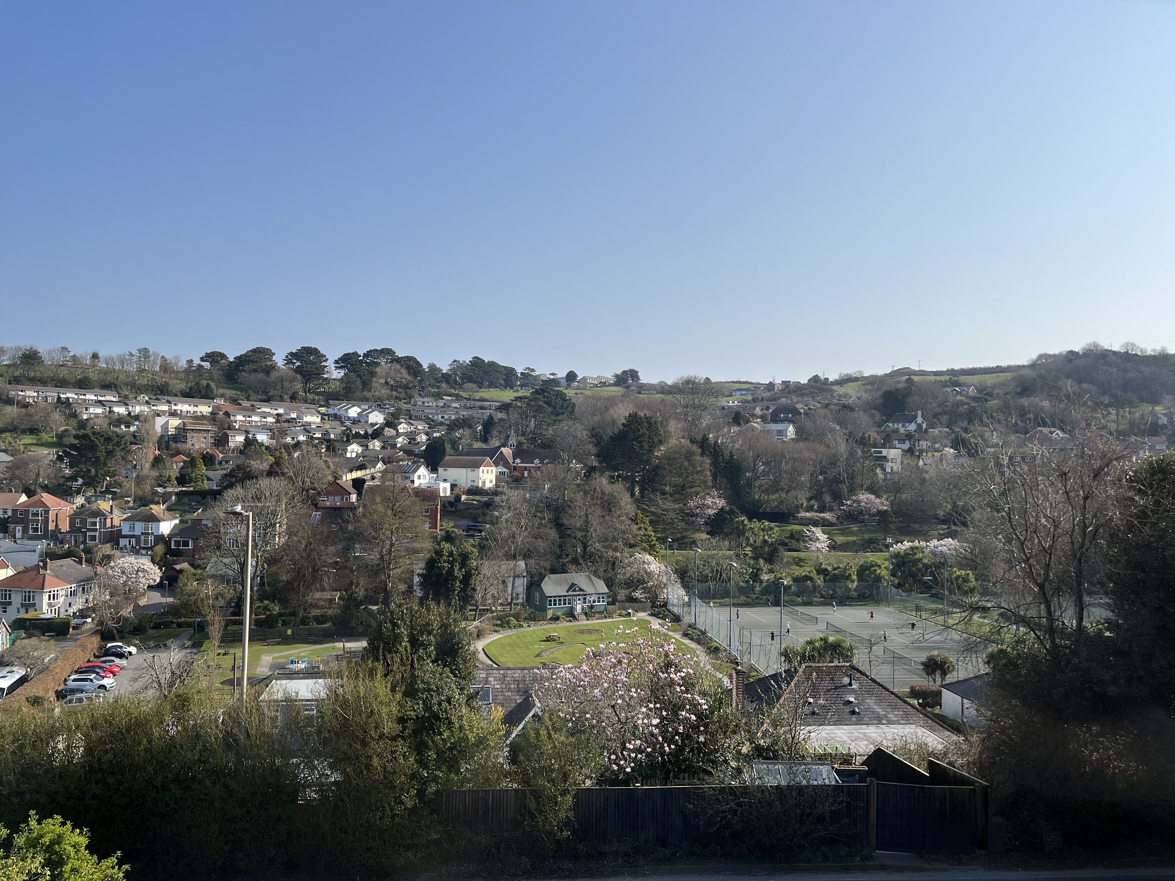 Un barrio residencial con casas, una cancha de tenis y una colina al fondo.