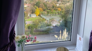 A window with a view of a residential area, a tennis court, and a building with a green roof. - Cairn House (Ilfracombe)