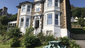 A two-story house with a bay window, stone facade, and a small garden with a wooden table. - Cairn House (Ilfracombe)