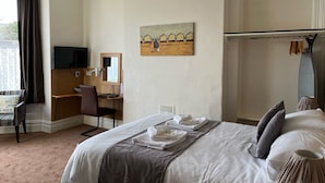 A hotel room with a bed, a desk, a chair, a TV, and a painting on the wall. - Cairn House (Ilfracombe)