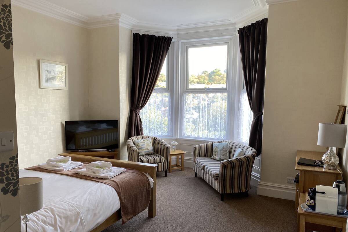 A hotel room with a bed, two armchairs, a TV, and a window with curtains.