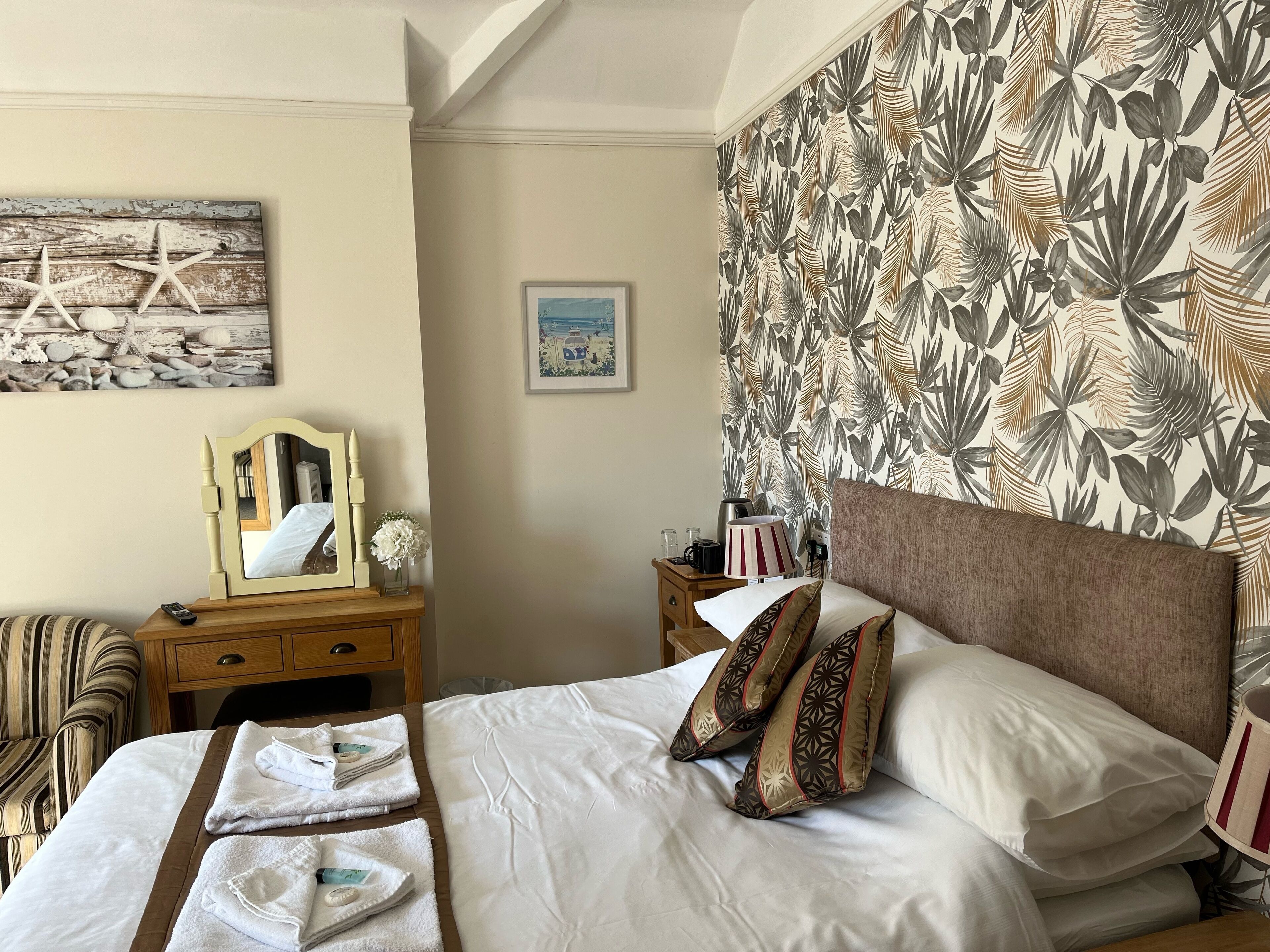A hotel room with a bed, a nightstand, a chair, and a wall with a tropical leaf pattern.