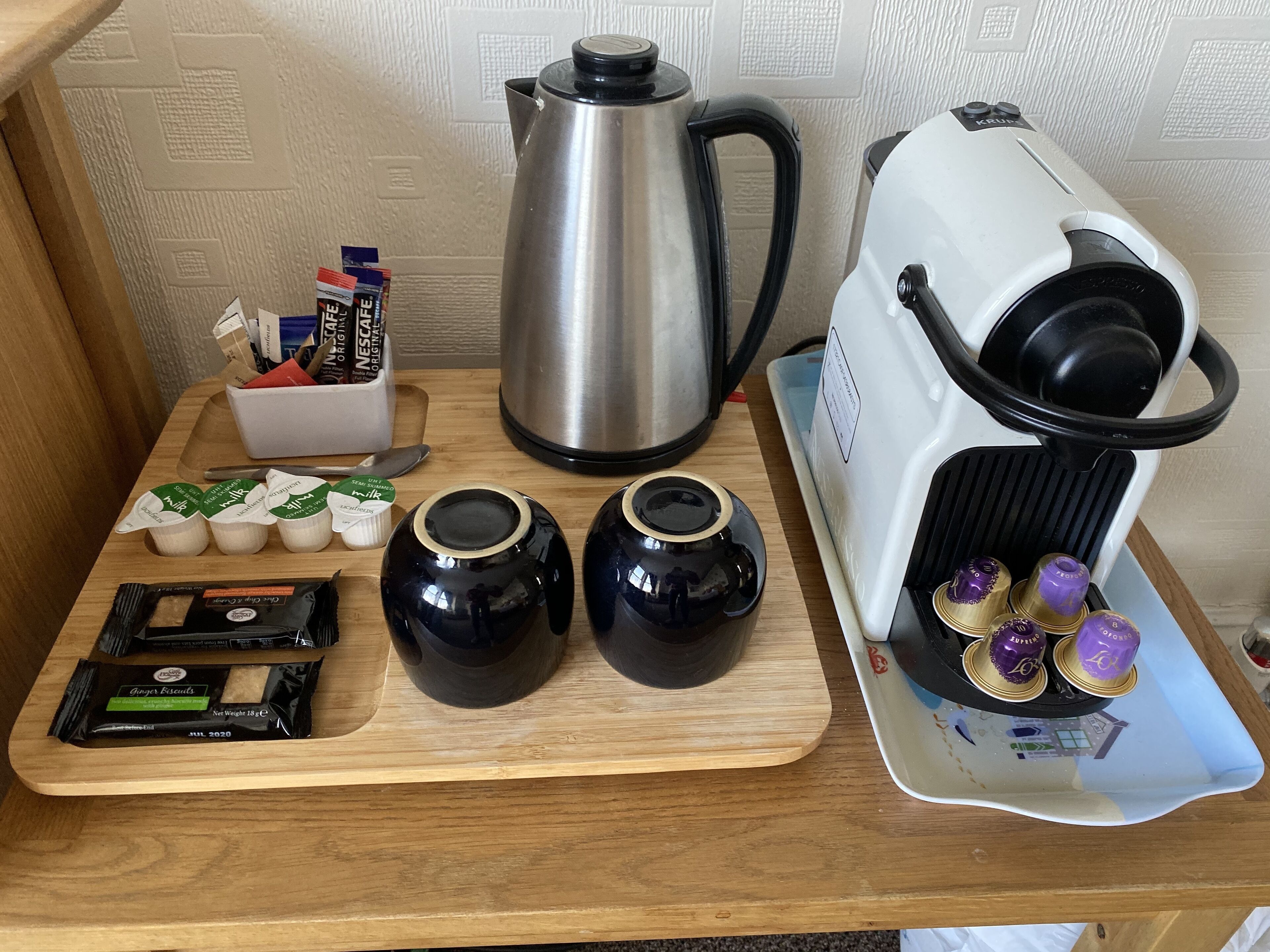 Un plan de travail de cuisine avec une machine à café, une bouilloire, une planche à découper et divers dosettes et récipients à café.