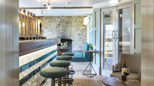 A bar area with stools, a stone wall, and a seating area with a table and chairs. - Old Stocks Inn (Cheltenham)