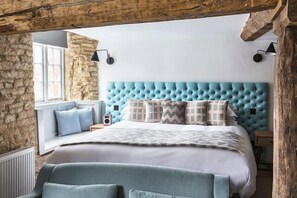 A bedroom with a tufted headboard, a large bed, a window with a view, and a stone wall.
