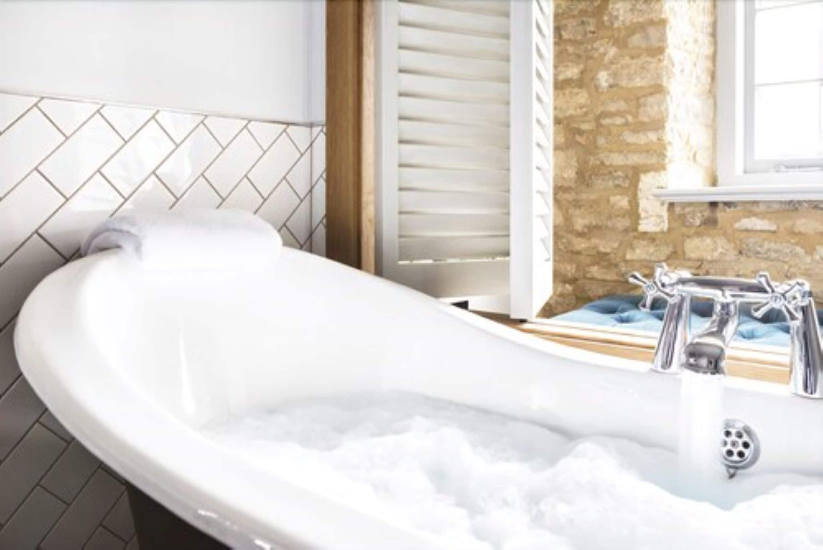 Eine mit Wasser gefüllte Badewanne, eine weiße Fliesenwand und ein Fenster mit Fensterläden.