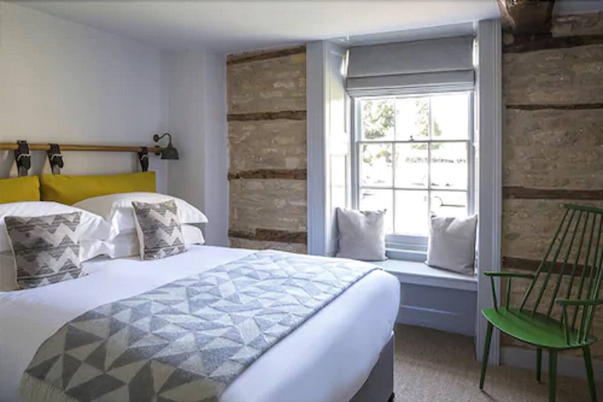 A bedroom with a bed, a window with a view, a green chair, and a wooden wall.