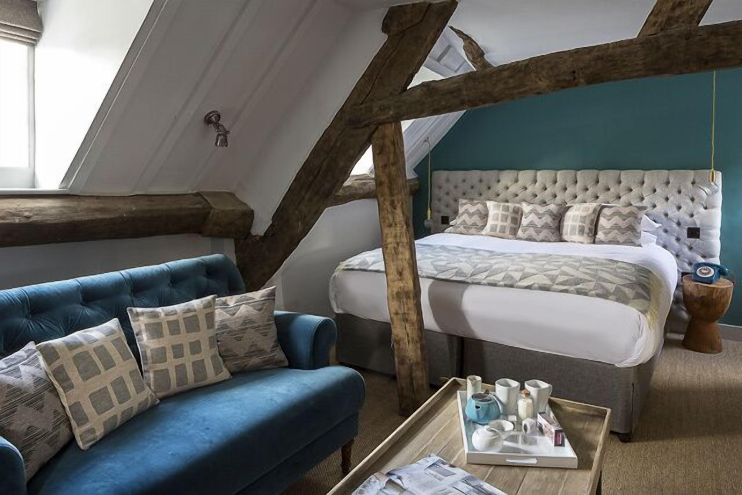 Une chambre avec un grand lit, un canapé bleu et une structure de poutres apparentes en bois au plafond.