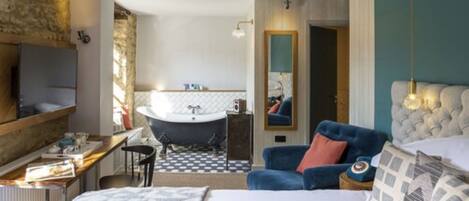 A bedroom with a large bed, a chair, a desk, a bathtub, and a mirror.