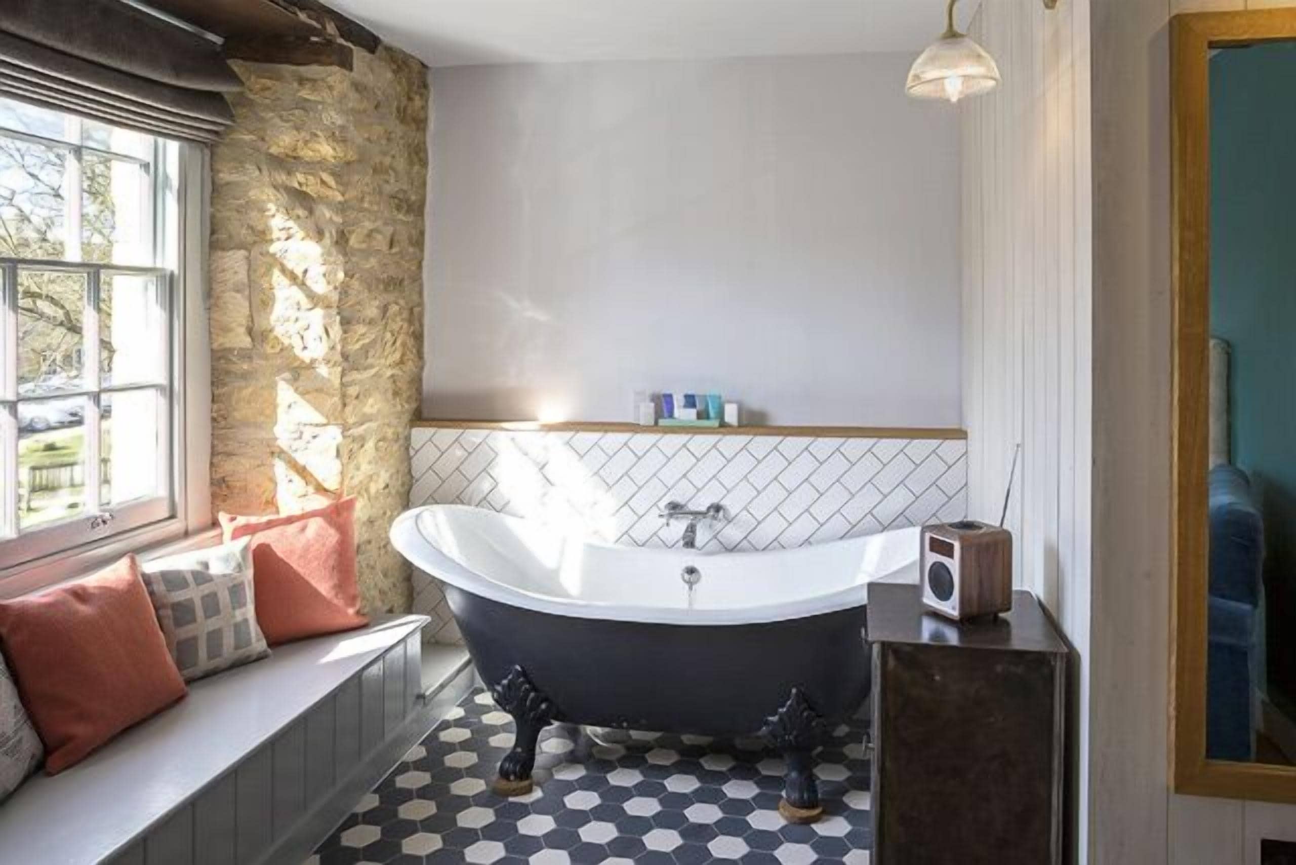 A bathroom with a freestanding bathtub, a stone accent wall, a window with a view, and a tiled floor.